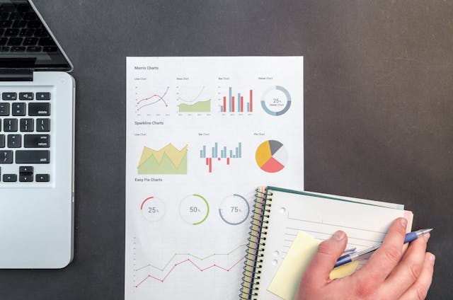 Person holding a blue ballpoint pen on a white notebook beside a page full of charts
